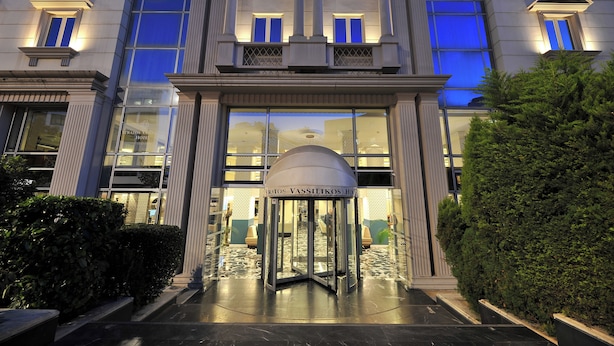 Entrada de hotel con puerta giratoria, amplias ventanas y seto cuidado.