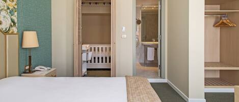Habitación de hotel con cama, lámpara de noche, cuna, armario y baño.