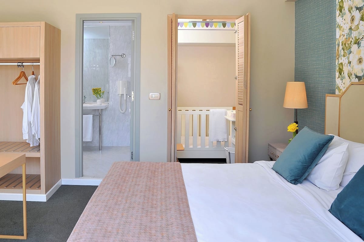 A hotel room with a bed, a desk, a wardrobe, a bathroom, and a nightstand with a lamp.