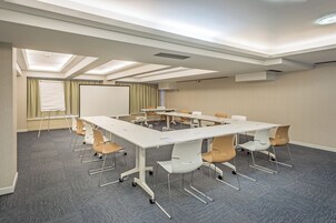 Uma sala de conferências com uma mesa branca, paredes bege e carpete cinza.