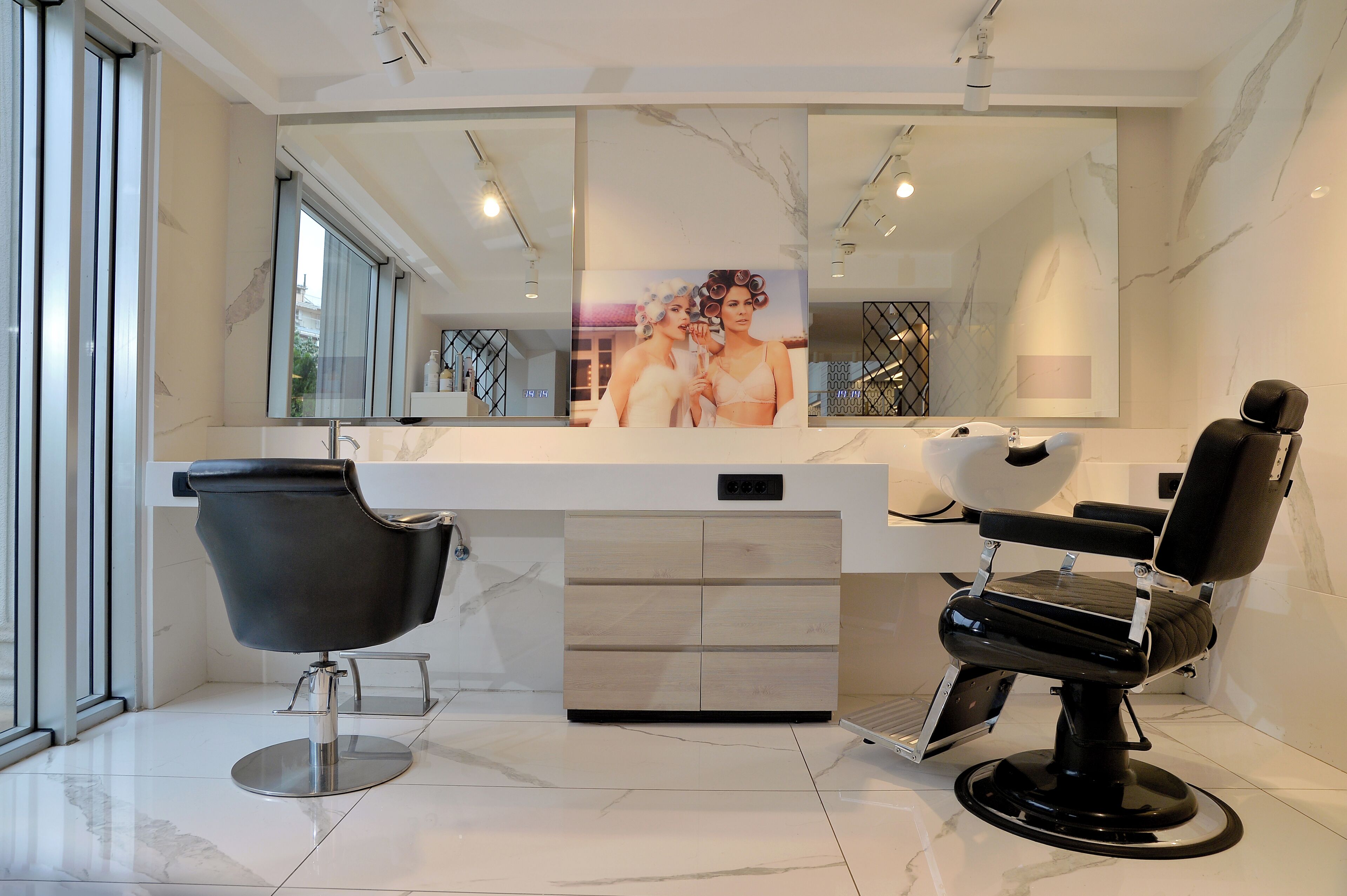 A modern salon with two black salon chairs, a large mirror, and a marble floor.
