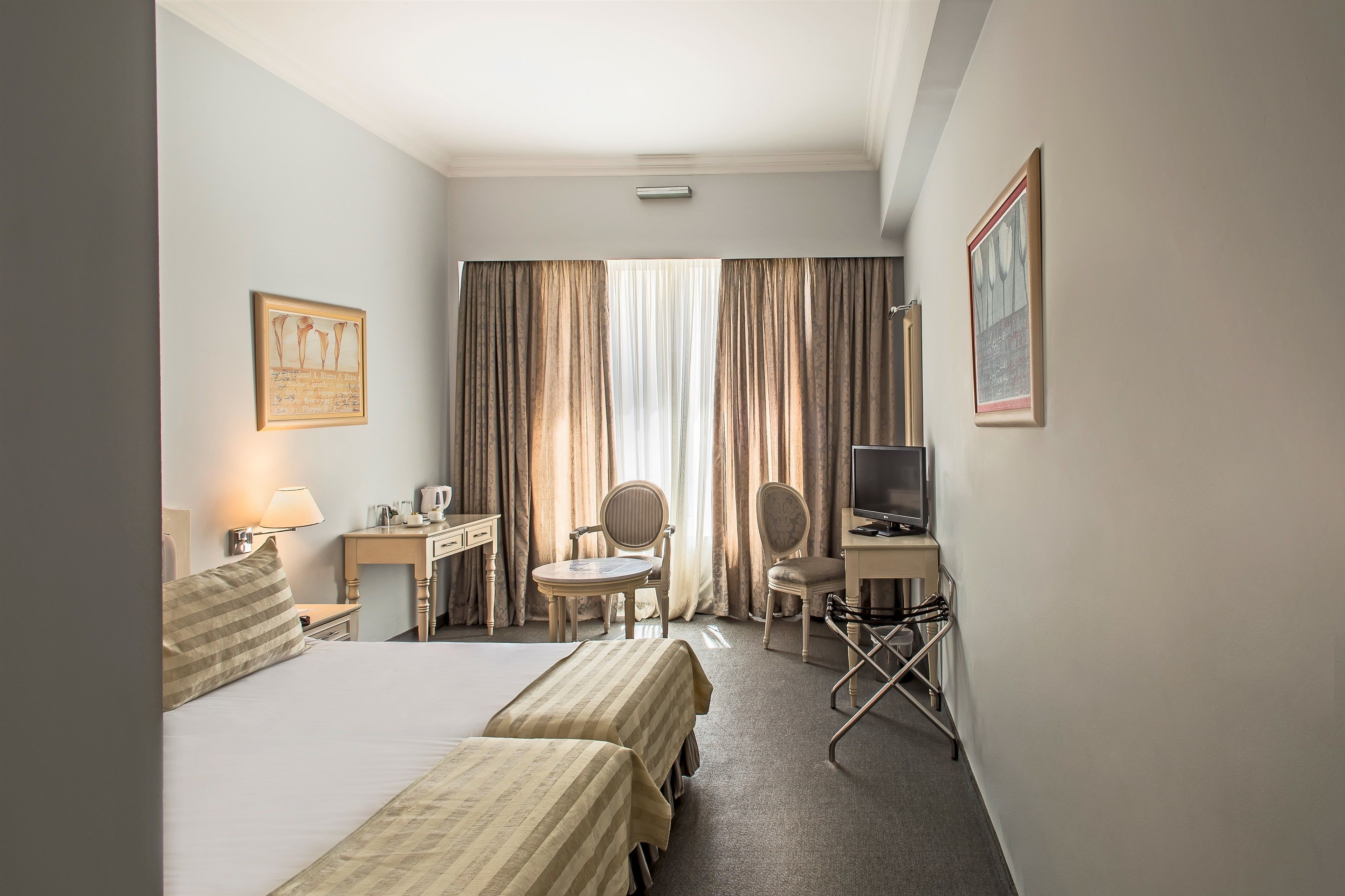 A hotel room with two beds, a desk, a chair, a television, and a window with curtains.