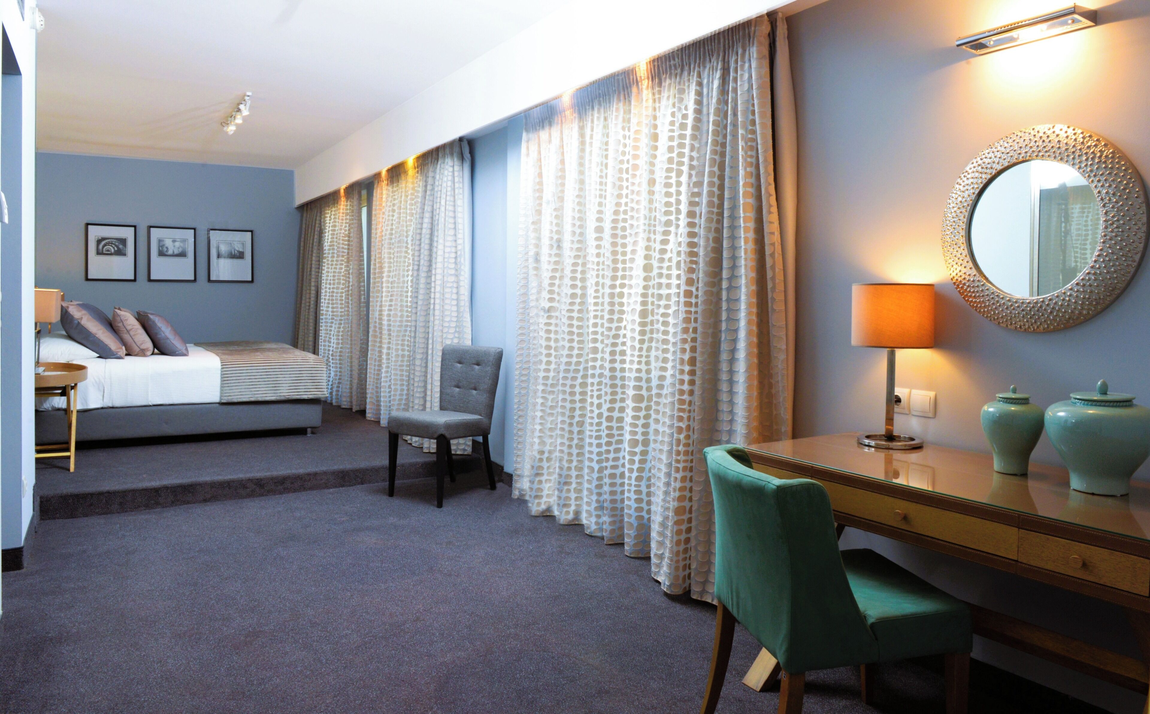 A hotel room with a bed, a desk, a chair, a lamp, and a mirror.