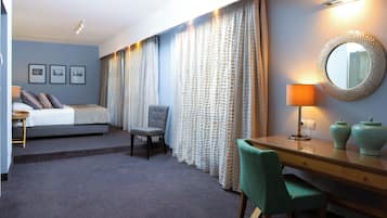 A hotel room with a bed, a desk, a chair, a lamp, and a mirror.