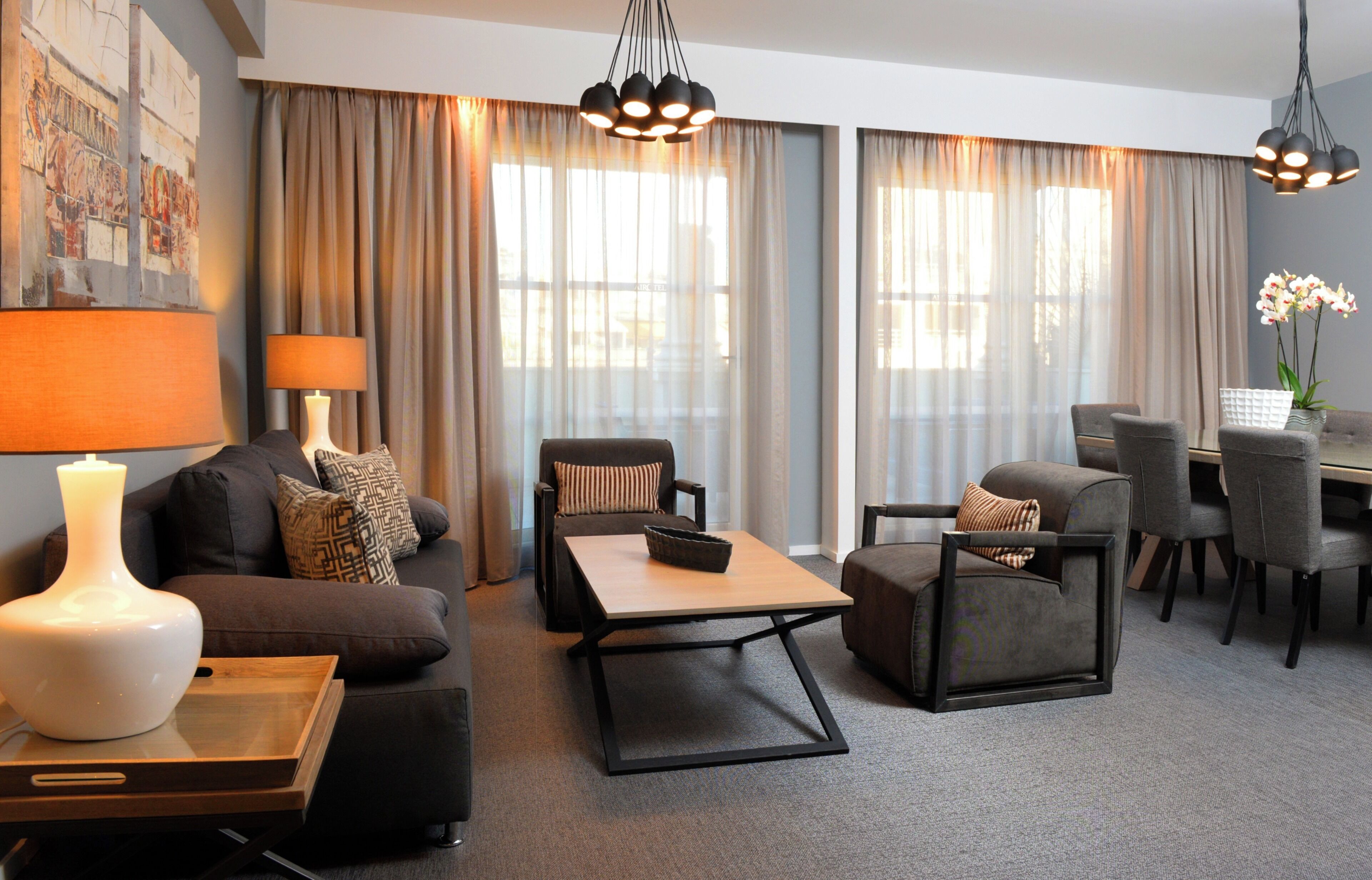 A modern living room with a sofa, armchair, coffee table, and dining area with chairs and a table.