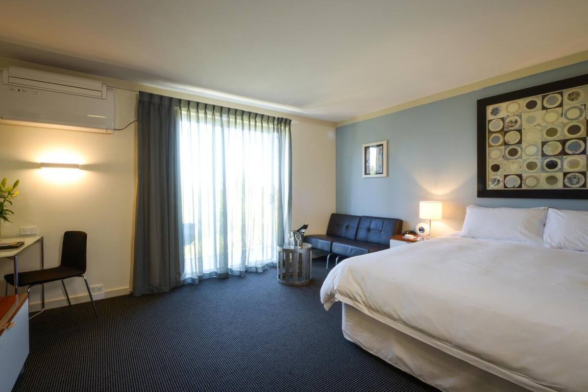 A hotel room with a large bed, a desk with a chair, a sofa, and a small table with a lamp.