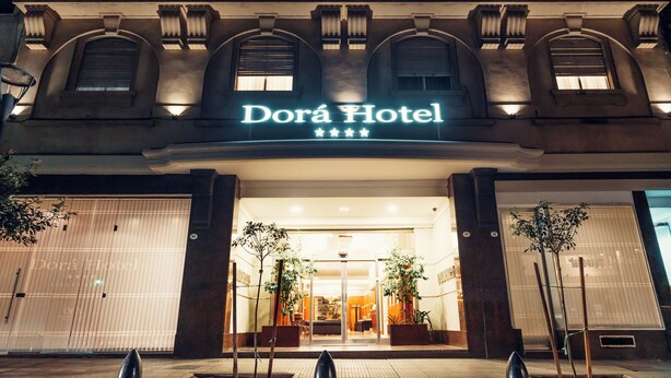 The Dorá Hotel facade at night with illuminated signage, large windows, and a symmetrical entrance. - Dorá Hotel Buenos Aires (Buenos Aires)