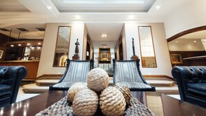 A spacious lobby with a high ceiling, two leather sofas, a coffee table with woven balls, and a view of the interior through a glass ceiling. - Dorá Hotel Buenos Aires (Buenos Aires)