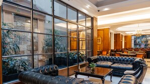 A spacious lounge area with leather sofas, a coffee table, and large windows offering views of indoor plants and a stone wall. - Dorá Hotel Buenos Aires (Buenos Aires)