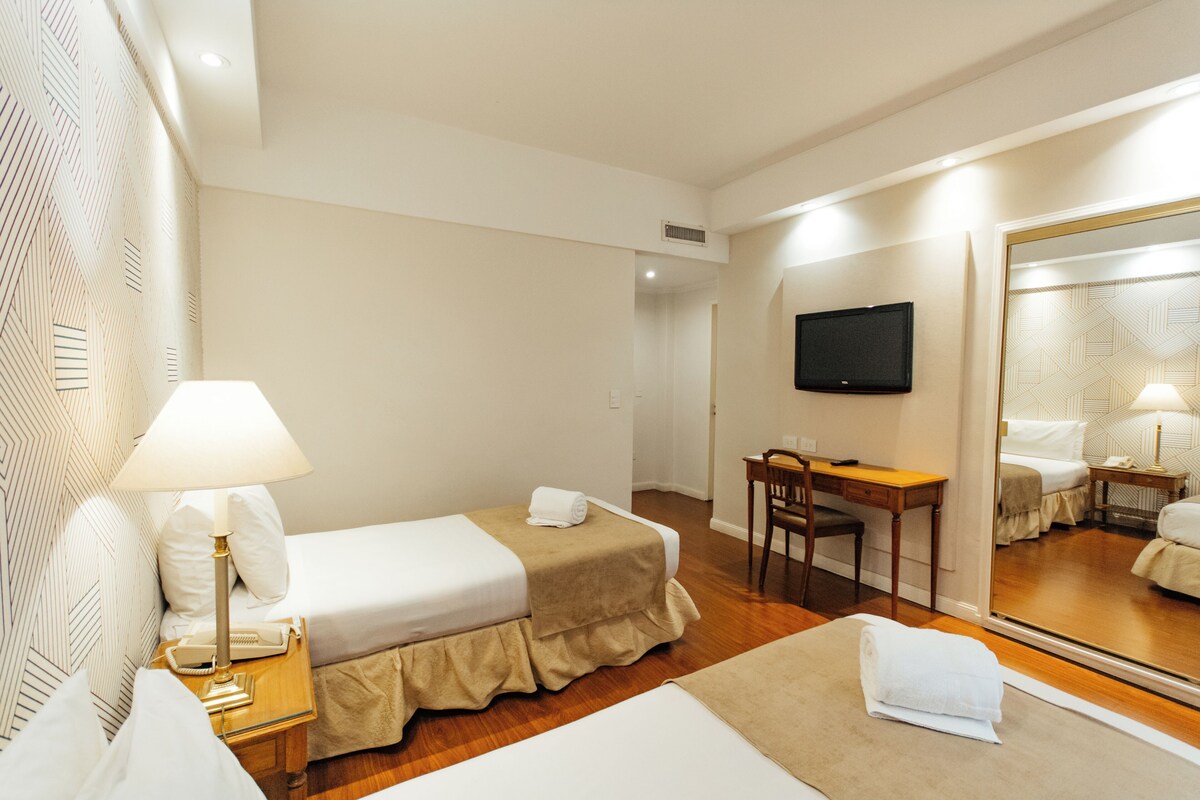 A hotel room with a bed, a desk, a chair, a television, and a large mirror.
