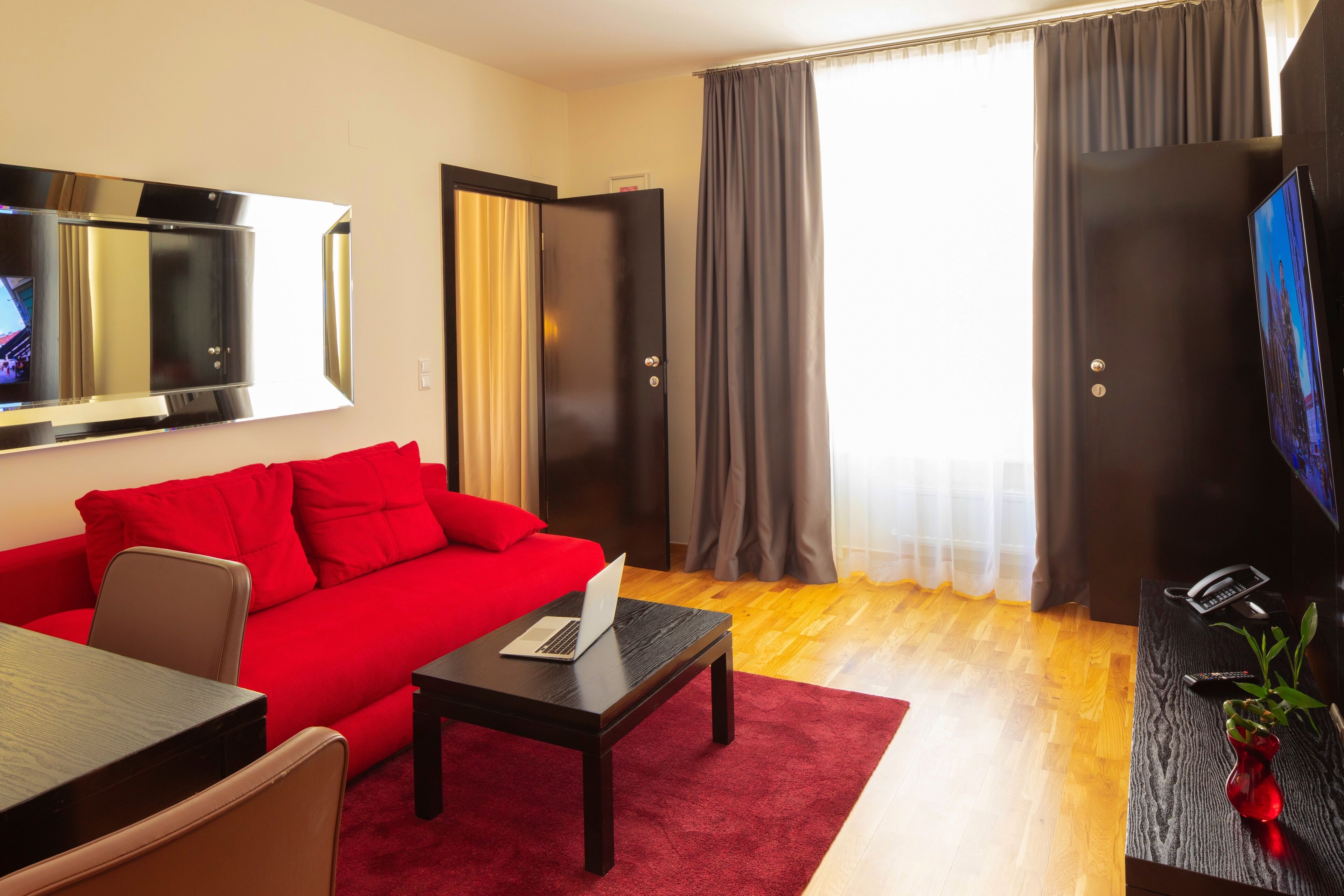 Una sala de estar moderna con un sofá rojo, una mesa de centro de madera, un televisor de pantalla plana y suelo de madera.