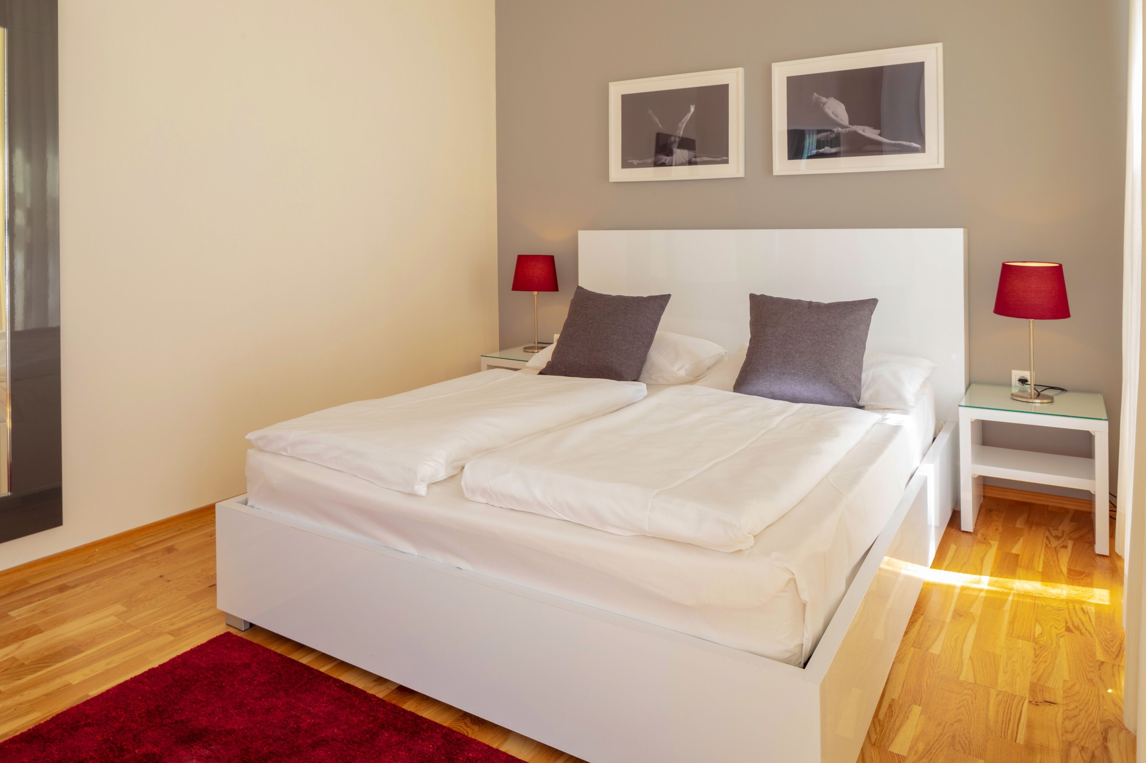Une chambre d’hôtel moderne avec un lit blanc, des lampes rouges et deux tableaux encadrés au mur.