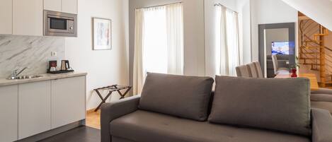 Uma sala de estar moderna com um sofá cinzento, uma mesa de centro e uma área de cozinha com micro-ondas.