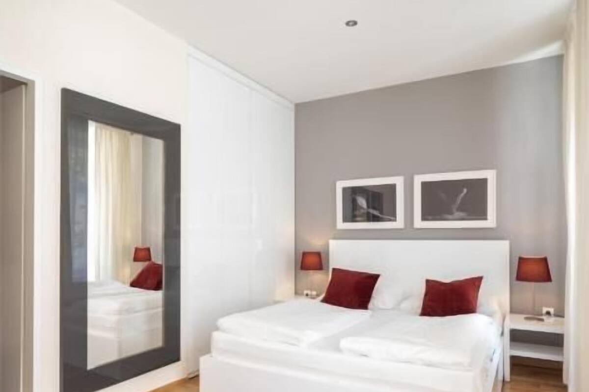 A modern bedroom with a large bed, two bedside tables, a mirror, and artwork on the wall.