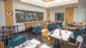 Un restaurante con varias mesas y sillas, un tragaluz y ventanas amplias.