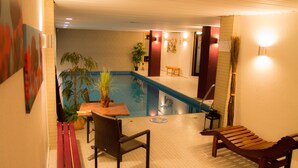 Zona de piscina interior con un banco, una silla y una mesa.