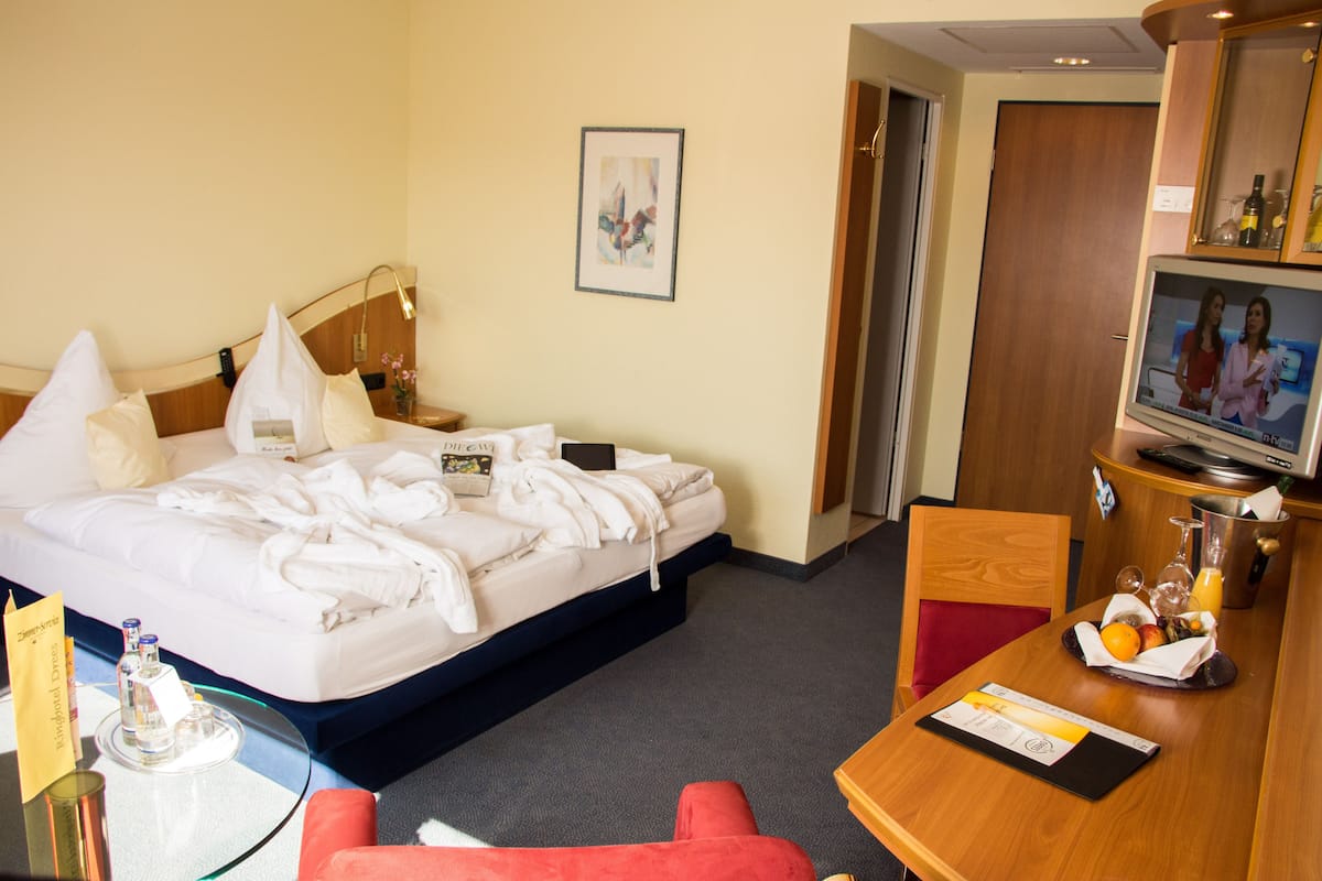 A hotel room with a bed, a desk with a computer, a chair, and a television.