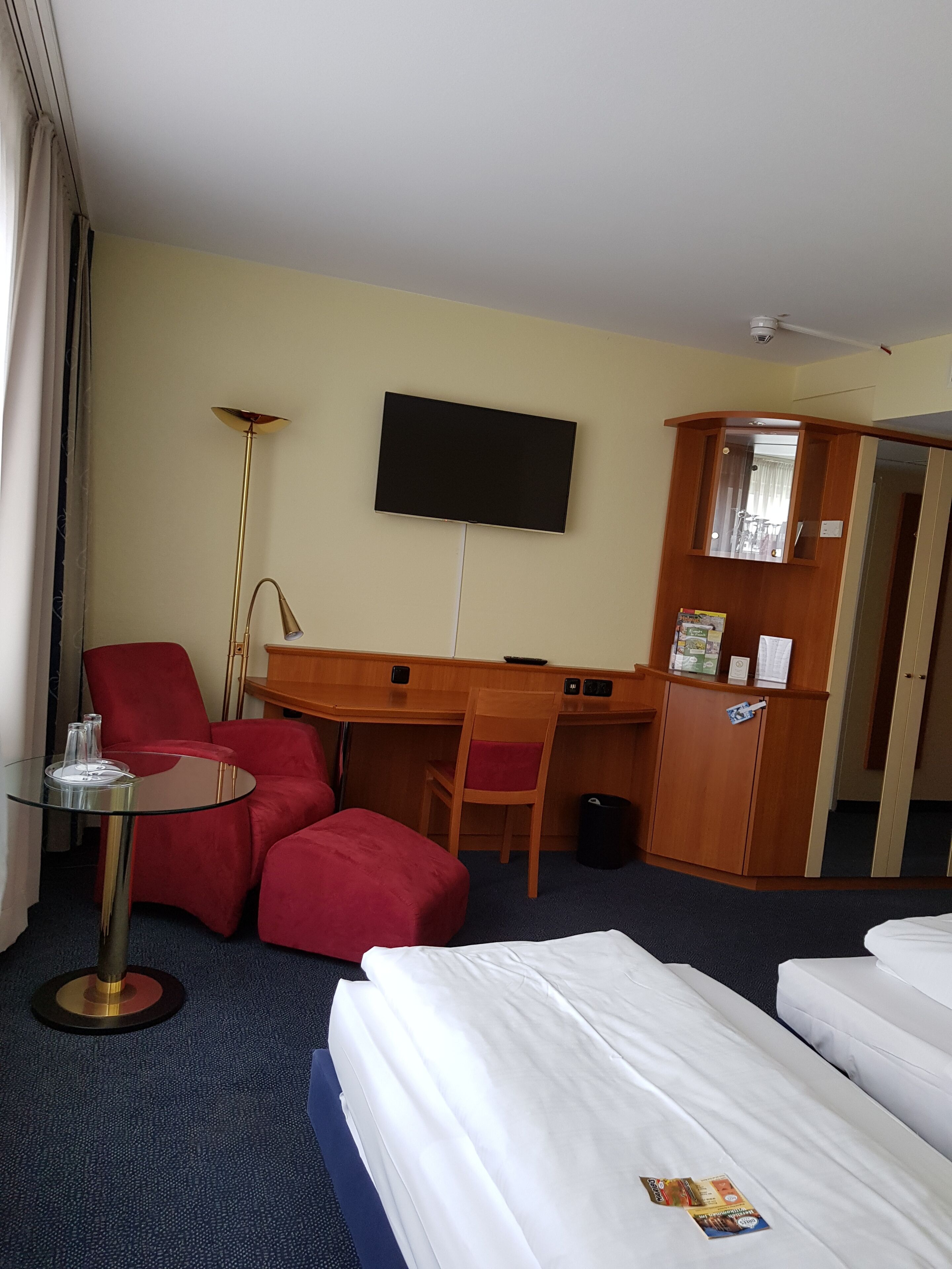 A hotel room with a bed, a desk, a chair, a TV, and a small table.