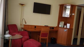 A hotel room with a bed, a desk, a chair, a TV, and a small table.