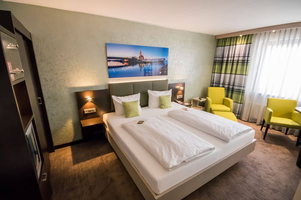 A hotel room with a large bed, two bedside tables, a chair, a desk, and a painting on the wall.