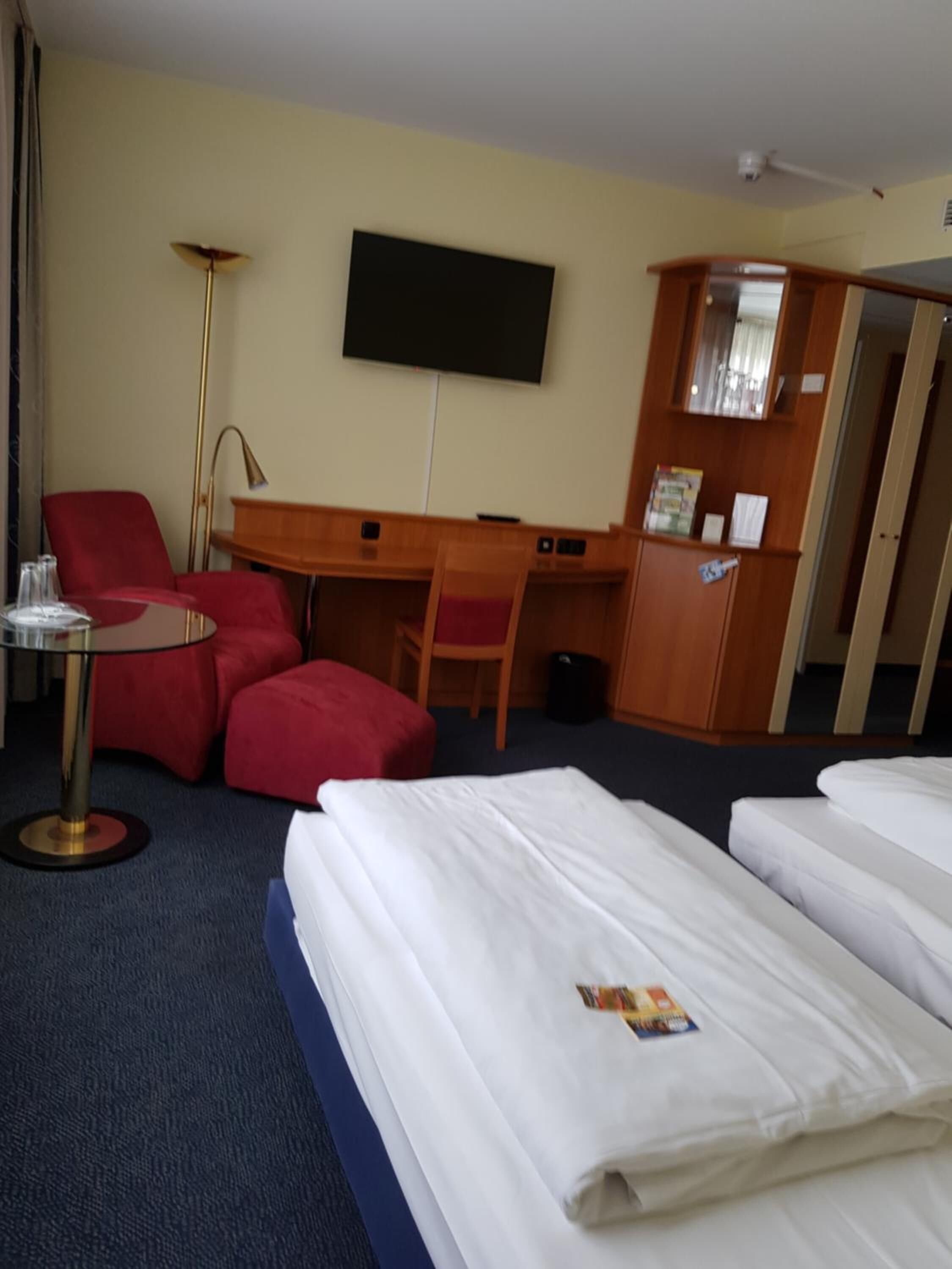 A hotel room with a bed, a desk, a chair, a TV, and a wardrobe.