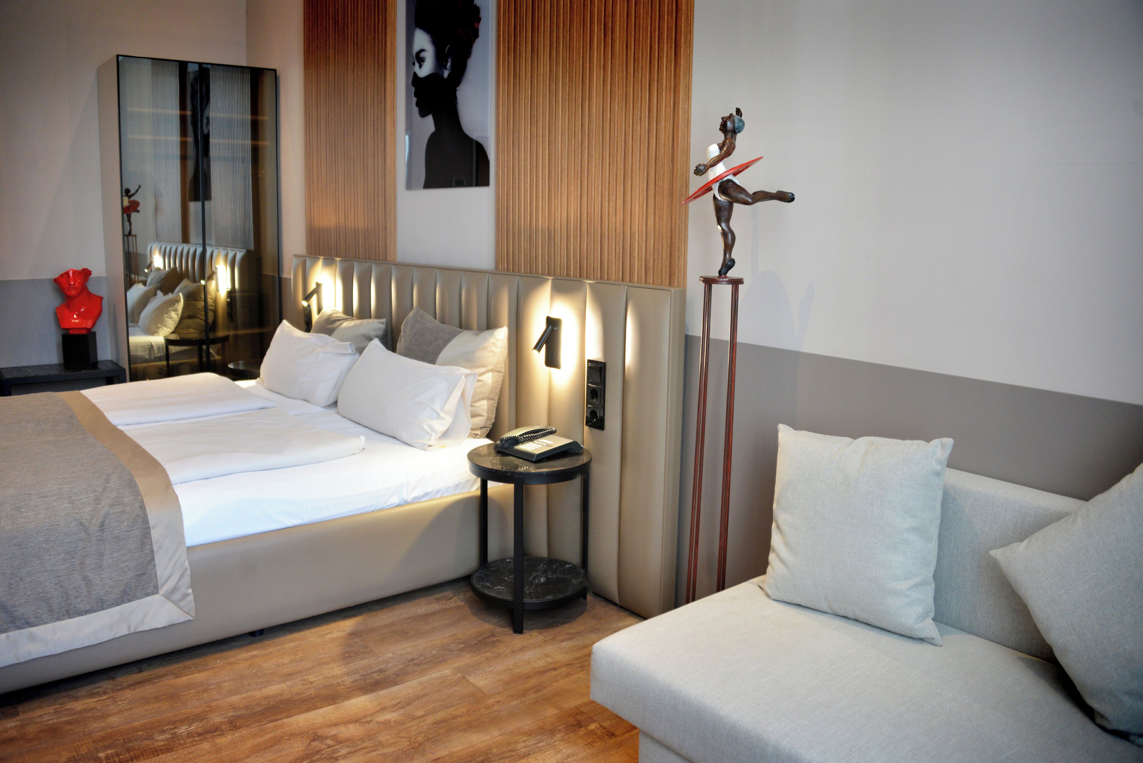 Una habitación de hotel moderna con una cama grande, un sofá, una mesita y un espejo.