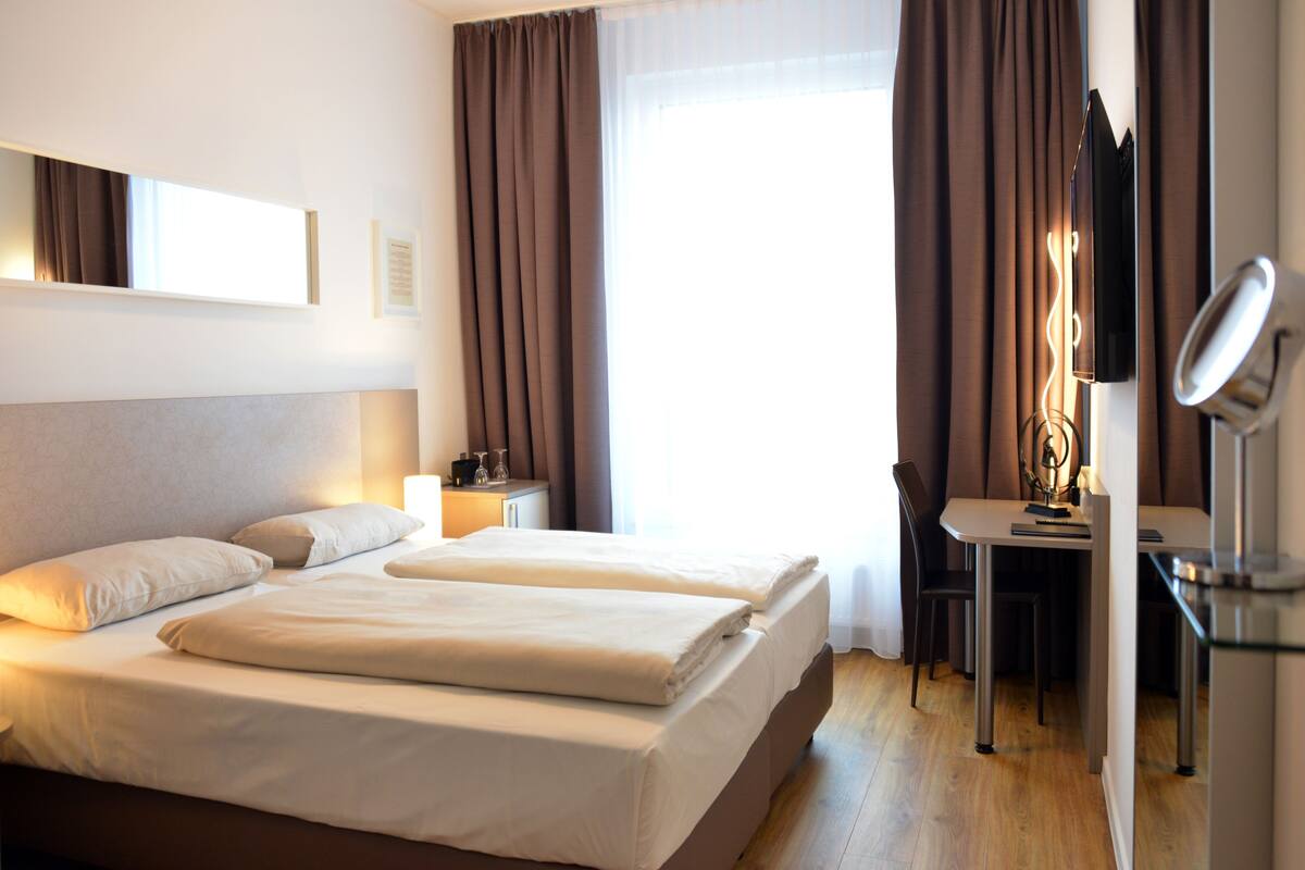 A hotel room with two beds, a desk, a chair, a mirror, and a window with curtains.