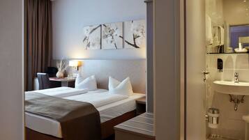 A hotel room with a bed, bedside table, lamp, and a wall with three framed artworks.