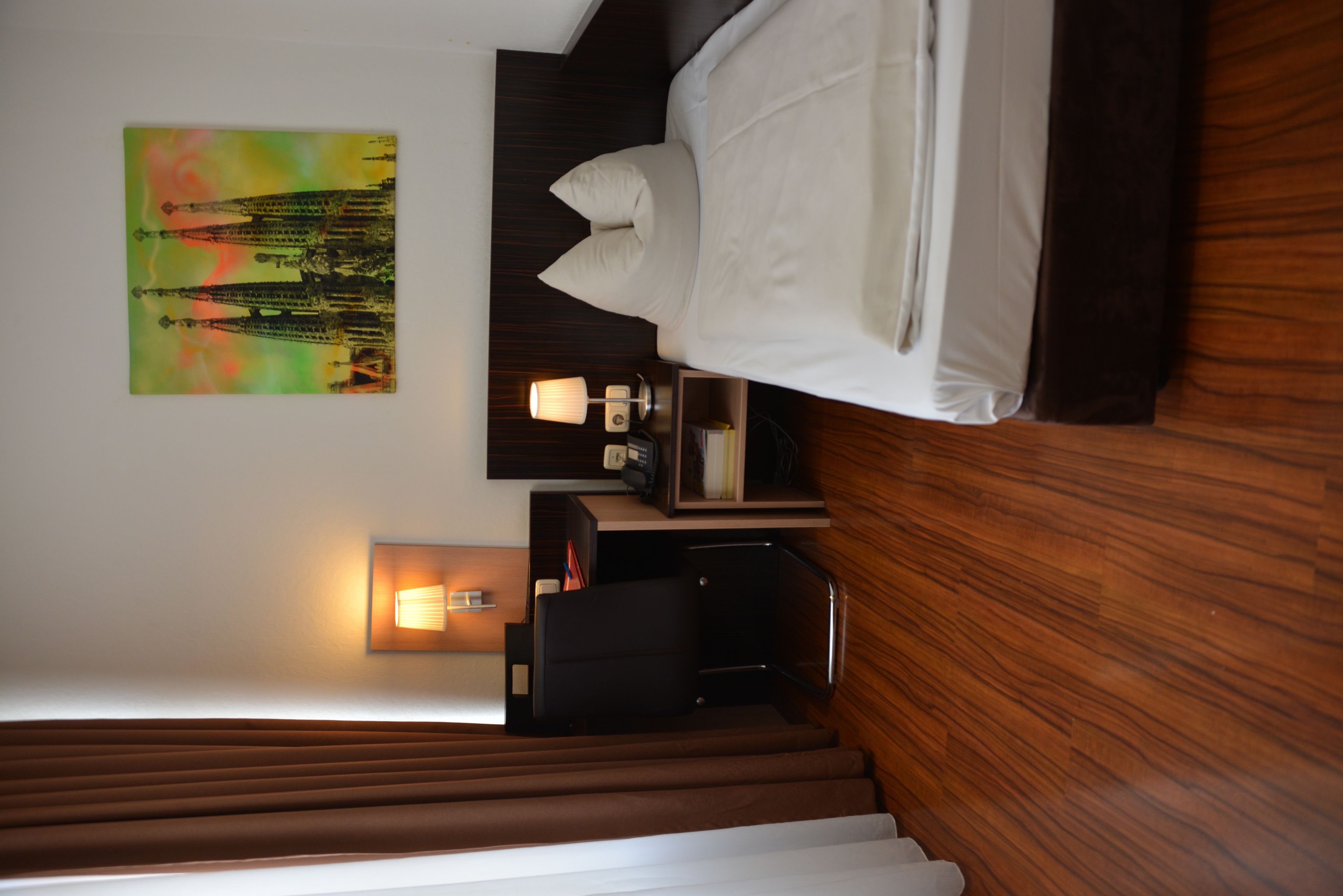 Una habitación de hotel con una cama, una mesita de noche, una lámpara y un cuadro en la pared.