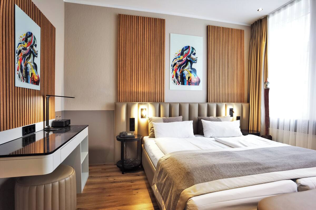 A modern hotel room with a large bed, a desk, and artwork on the walls.
