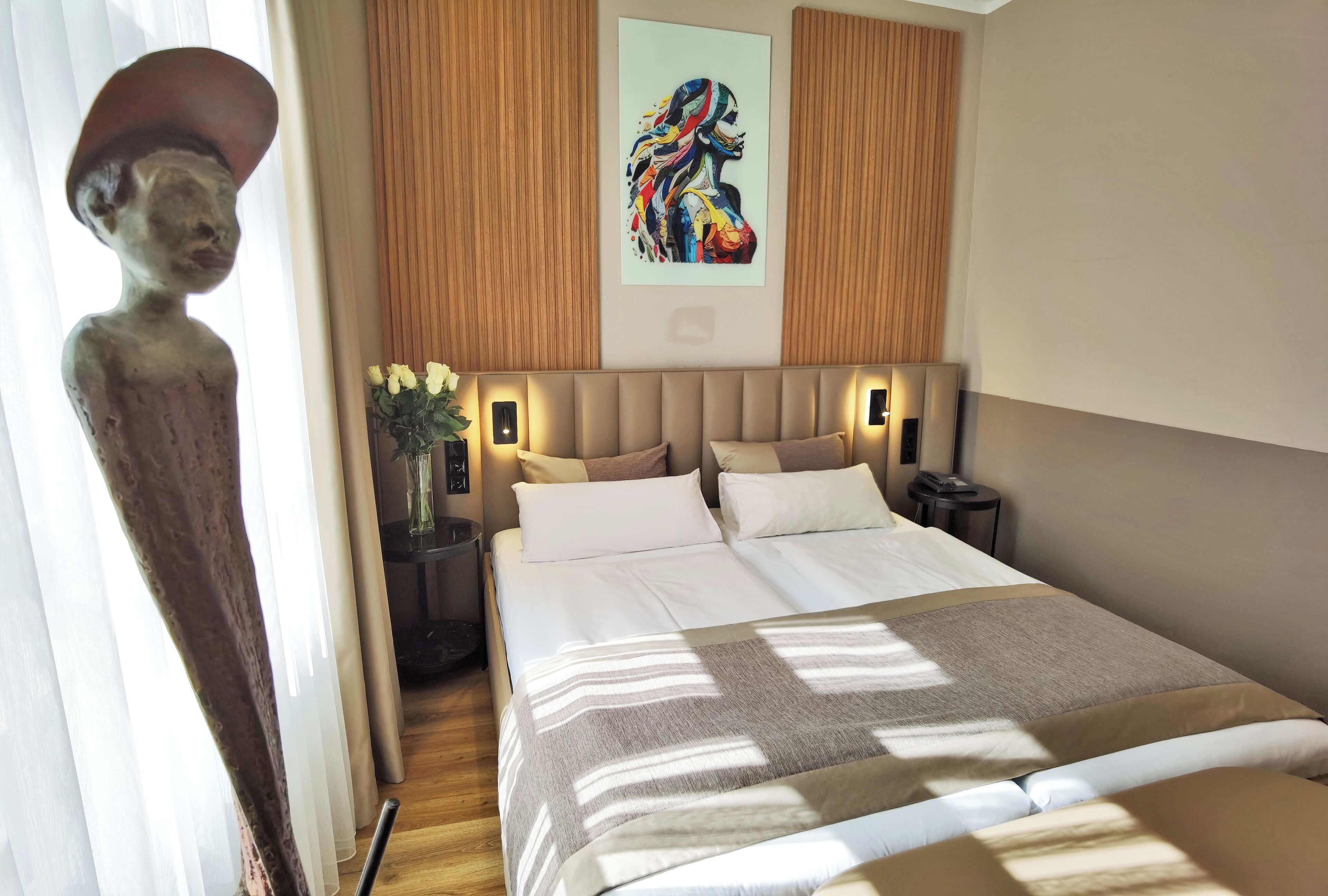 Ein Hotelzimmer mit einem großen Bett, einem Nachttisch, einer Blumenvase und einem Bild an der Wand.