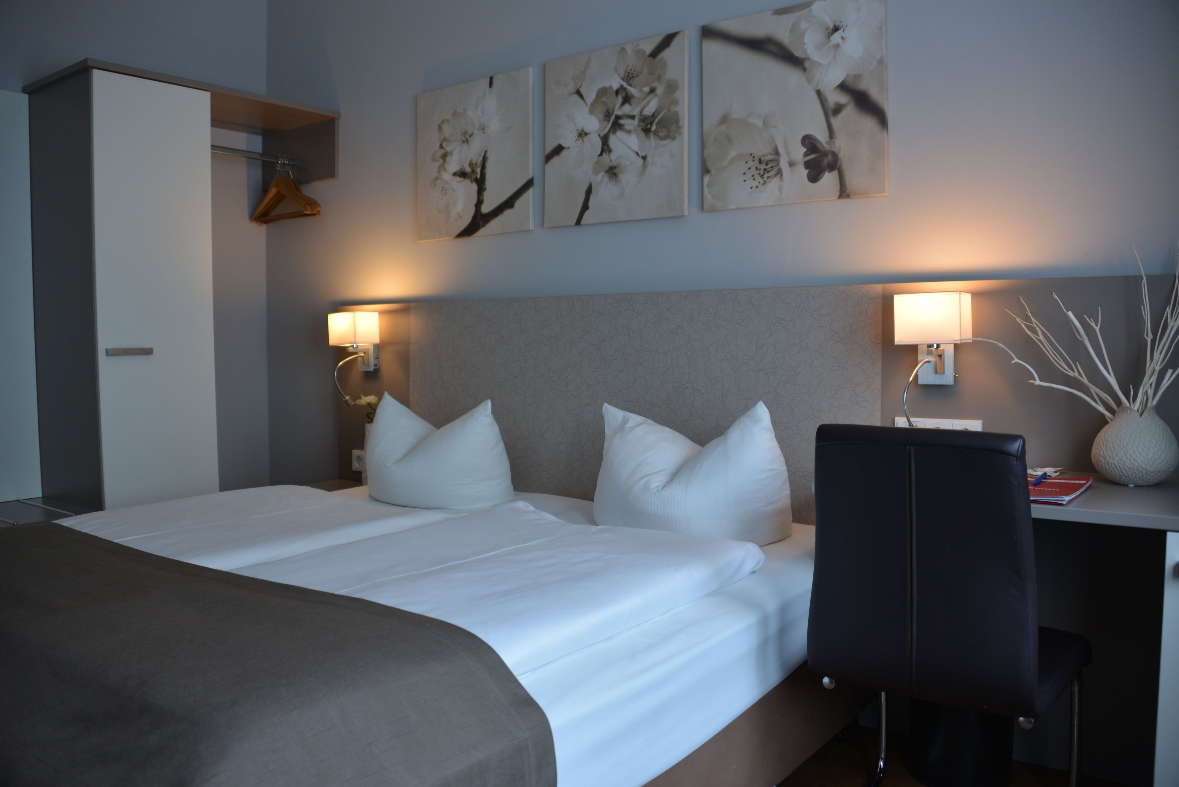 Et hotelværelse med seng, skrivebord, stol og billedkunst på væggen.