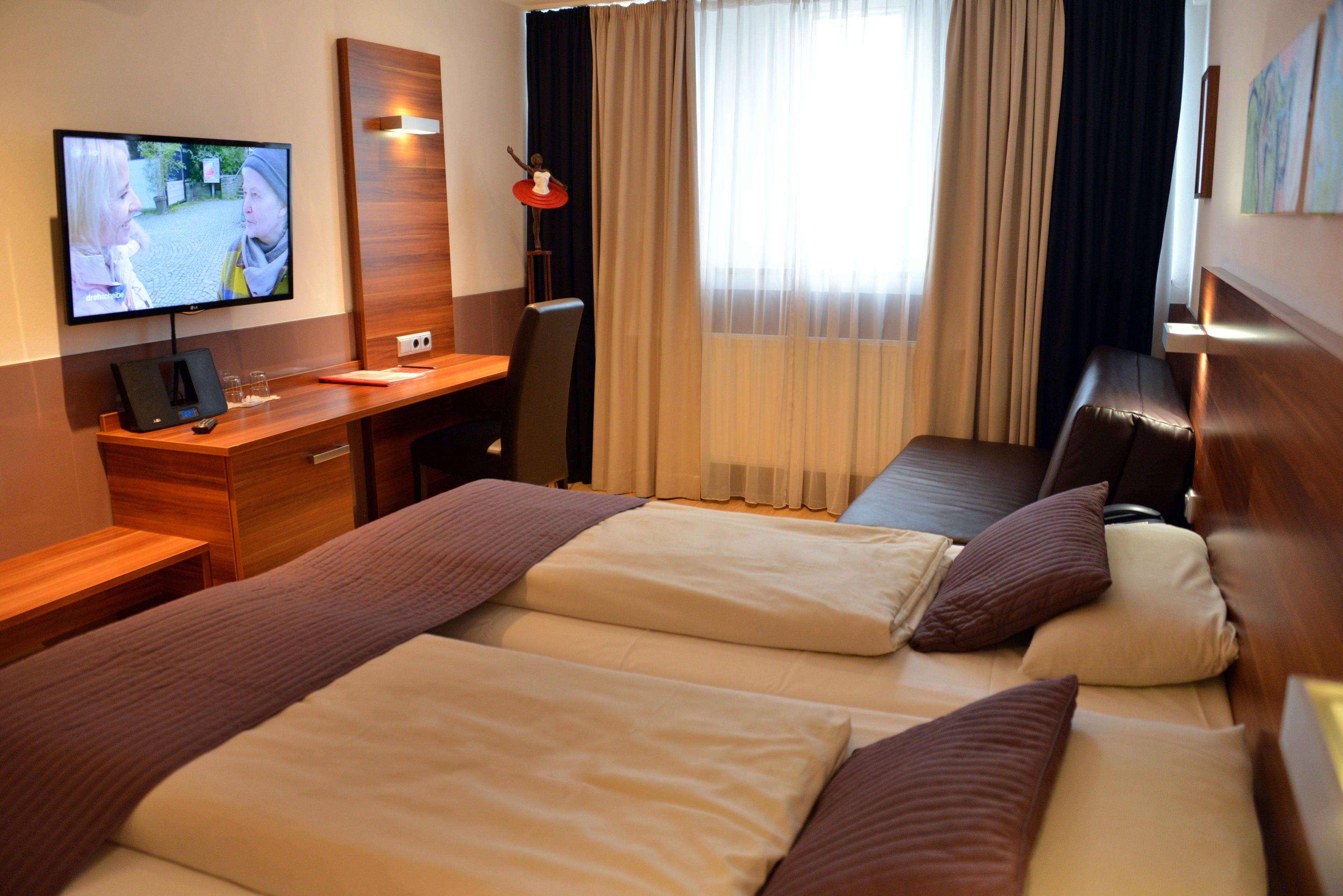 Habitación de hotel con dos camas, un escritorio, un televisor y una ventana con cortinas.