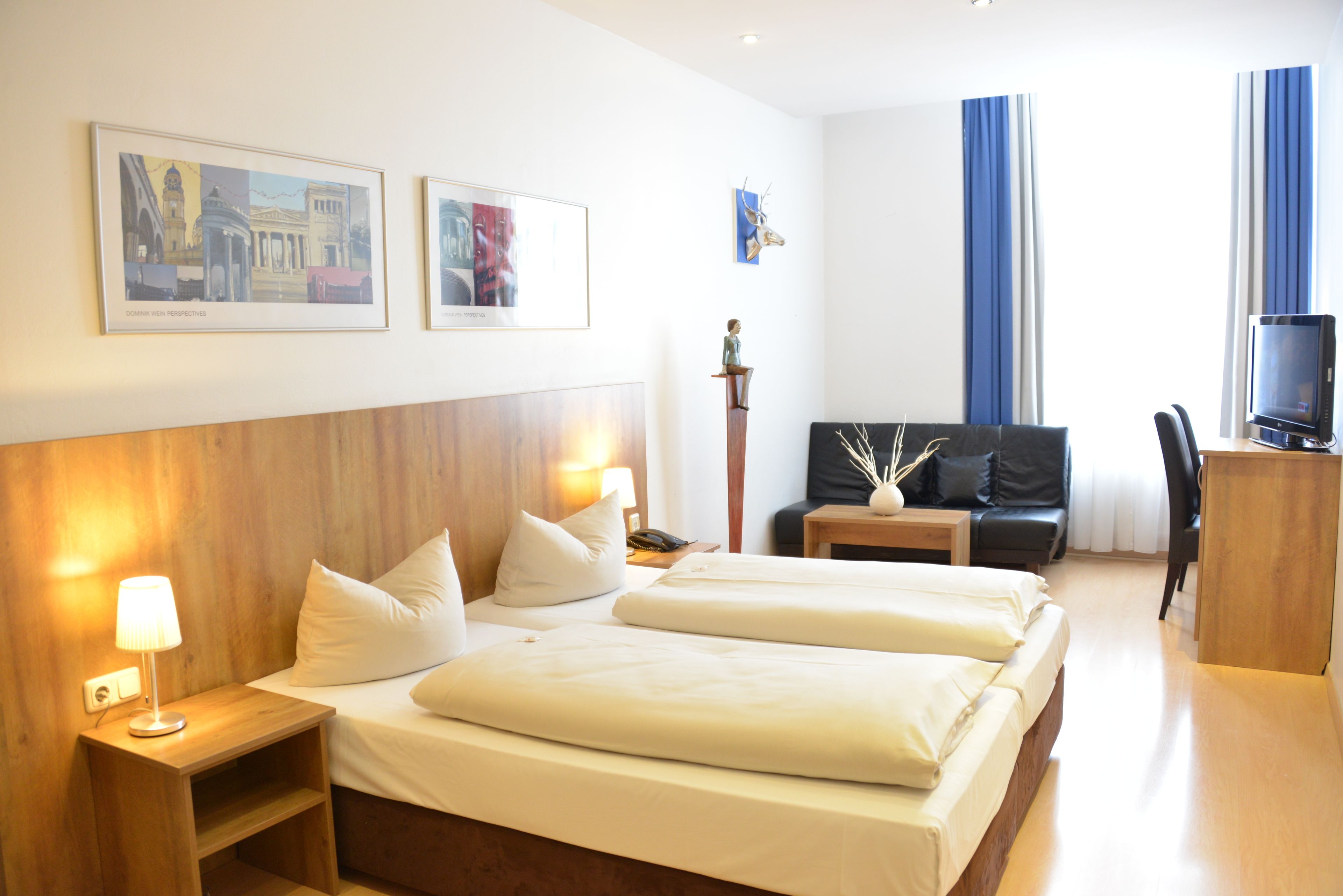 Ein Hotelzimmer mit zwei Betten, einem Schreibtisch, einem Sessel, einem Fernseher und Bildern an der Wand.
