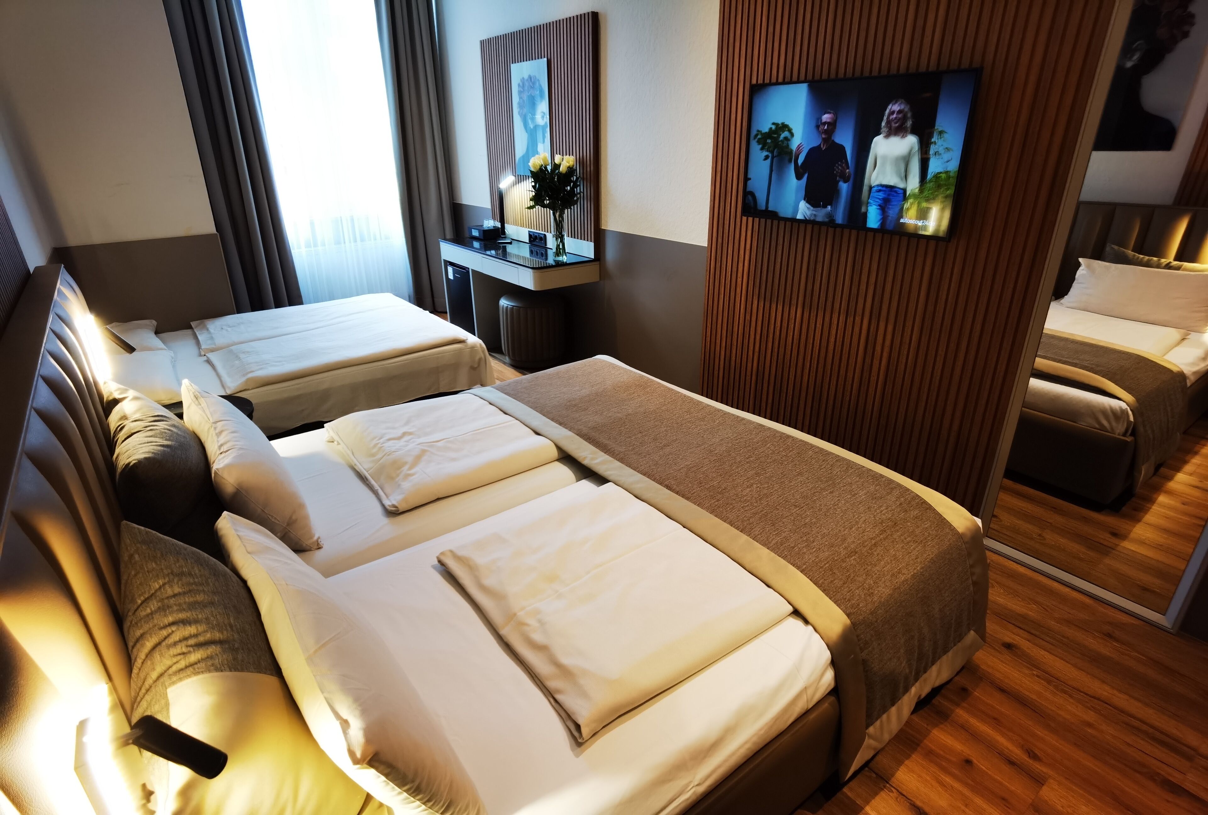 Une chambre d’hôtel avec deux lits, une télévision, un bureau avec un miroir et un mur recouvert de panneaux en bois.