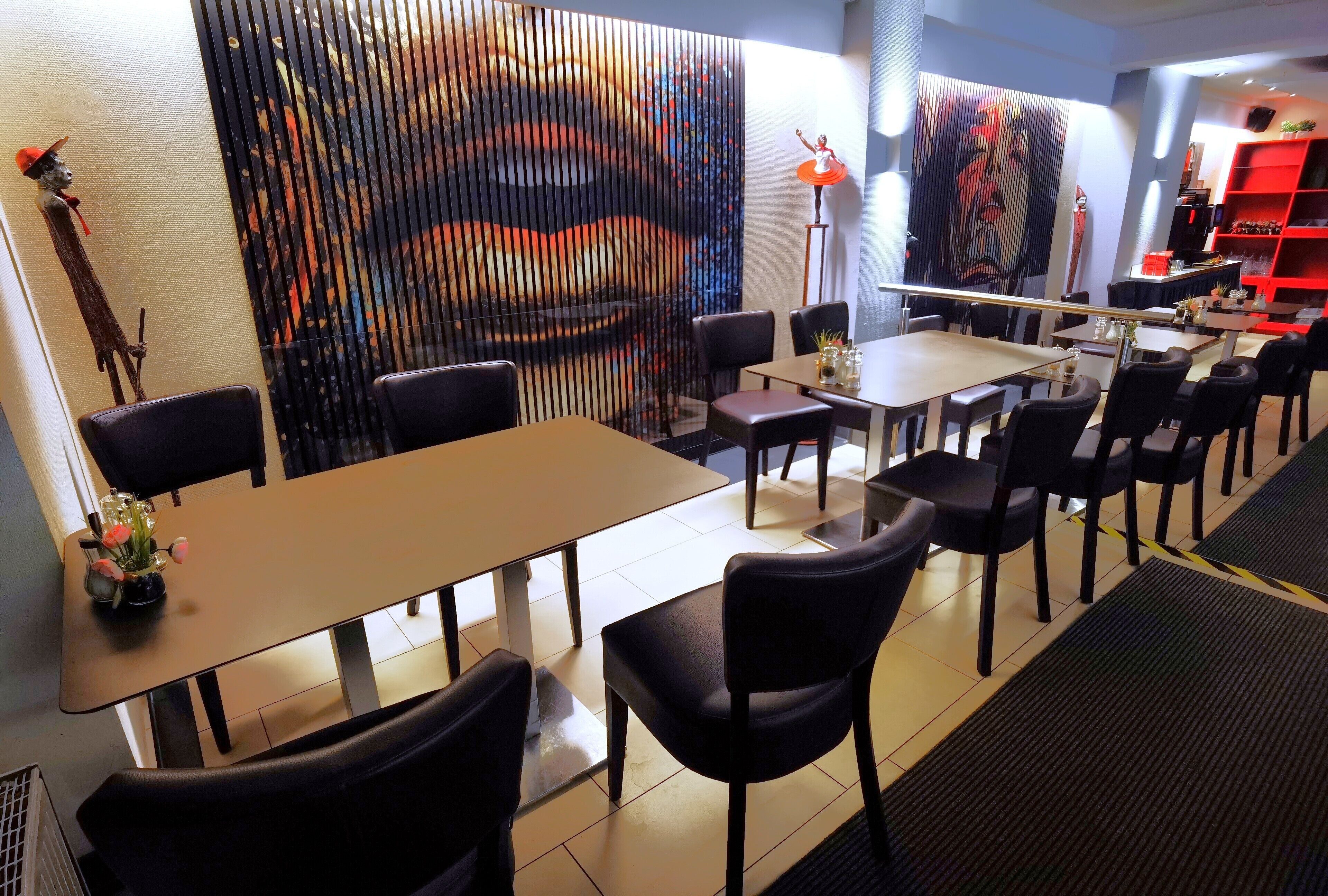 Ein Restaurant mit Tischen und Stühlen, einer Wand mit einem großen Gemälde und einem roten Regal mit Flaschen.