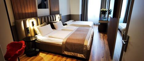 A hotel room with two beds, a wooden floor, a large mirror, a red sculpture, and a wall-mounted artwork.