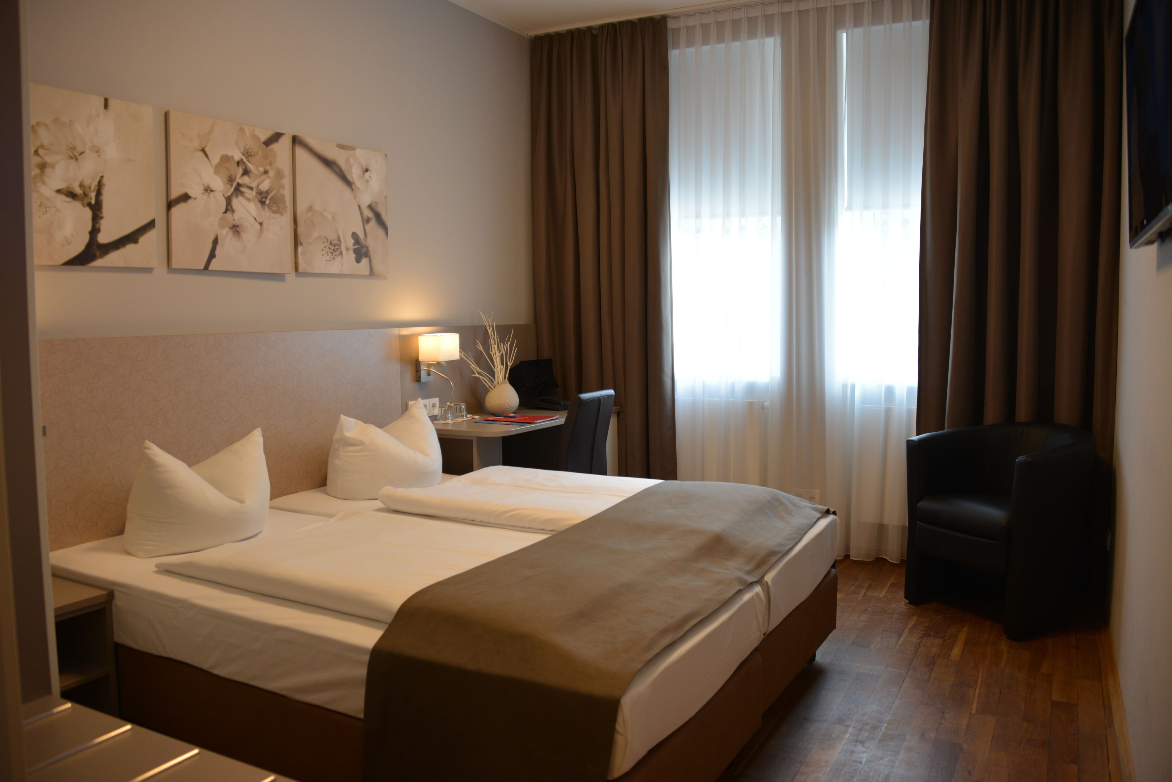 Ein Hotelzimmer mit einem großen Bett, einem Schreibtisch mit Lampe, zwei Stühlen und Bildern an der Wand.