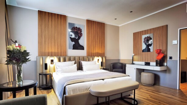 A modern hotel room with a large bed, bedside tables, a bench, a chair, and artwork on the walls. - Arthotel Munich (Munich)