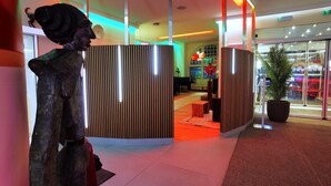 A modern hotel lobby with a curved reception desk, a large potted plant, and a statue. - Arthotel Munich (Munich)