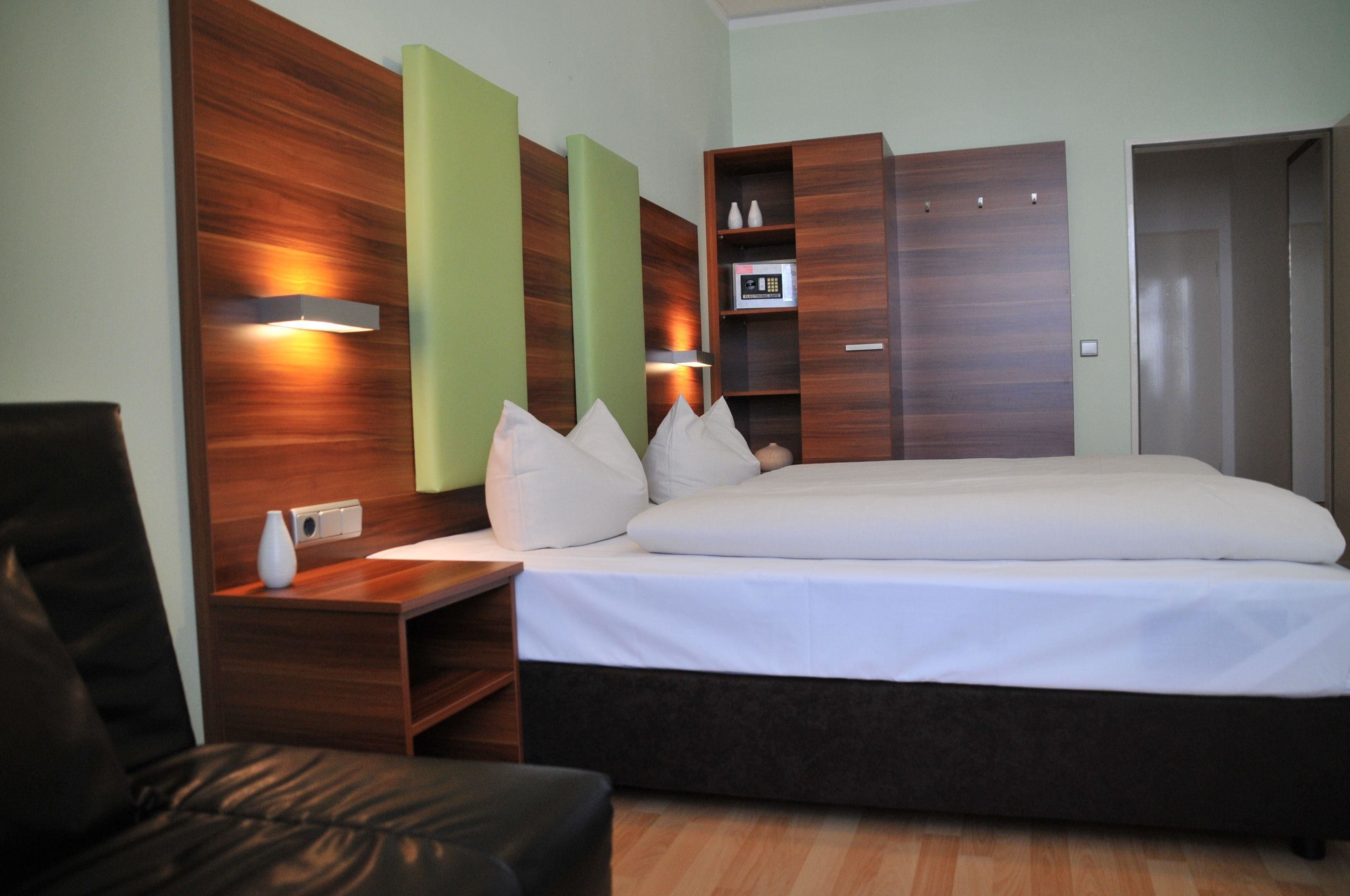 Una habitación de hotel moderna con una cama grande, cabecera de madera, mesitas de noche, un escritorio y un armario.