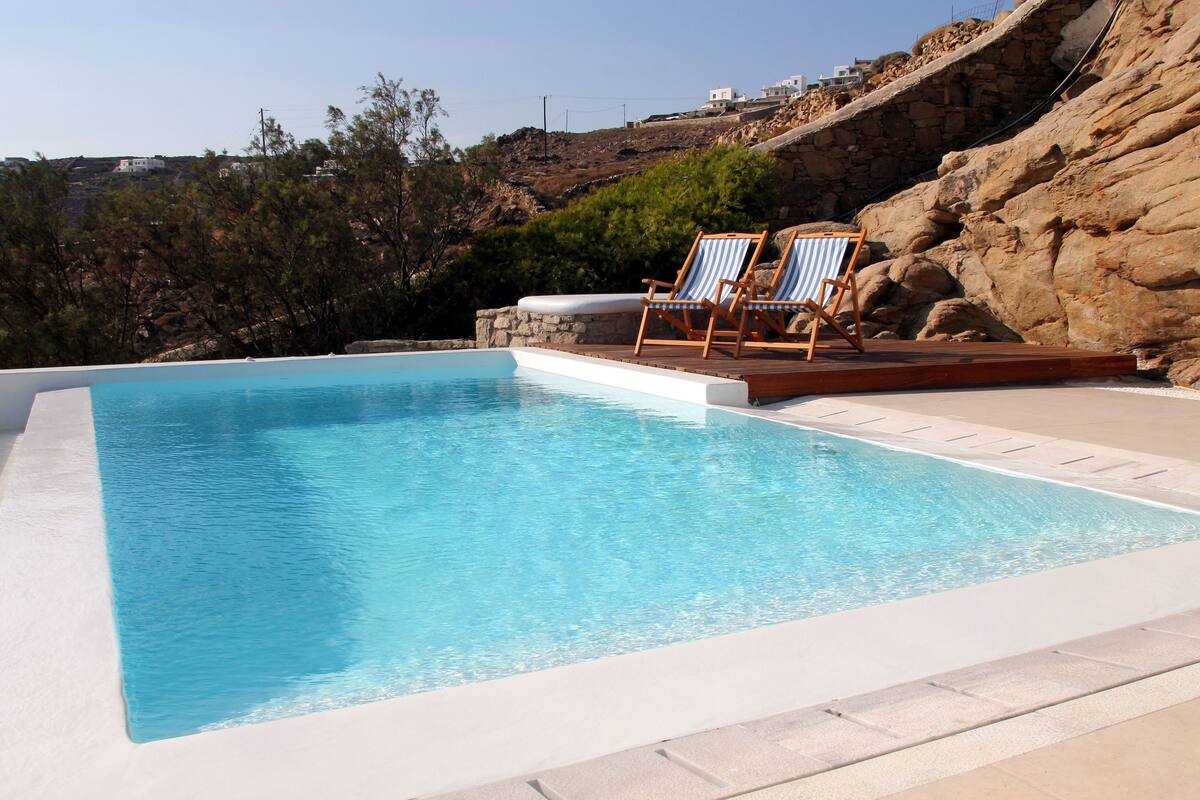 A rectangular swimming pool with two lounge chairs on a wooden deck.