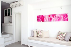 A modern interior with a white sofa set, a large floral artwork on the wall, and a staircase leading to a kitchen area.