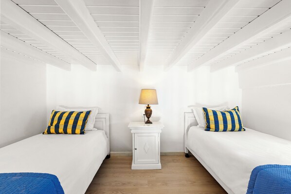 A room with two beds, a nightstand with a lamp, and a wooden floor. - San Marco Hotel (Mykonos)