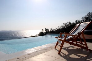 Ein Pool ohne Ende mit einer Holzterrasse und Liegestühlen, mit Blick auf ein Gewässer.
