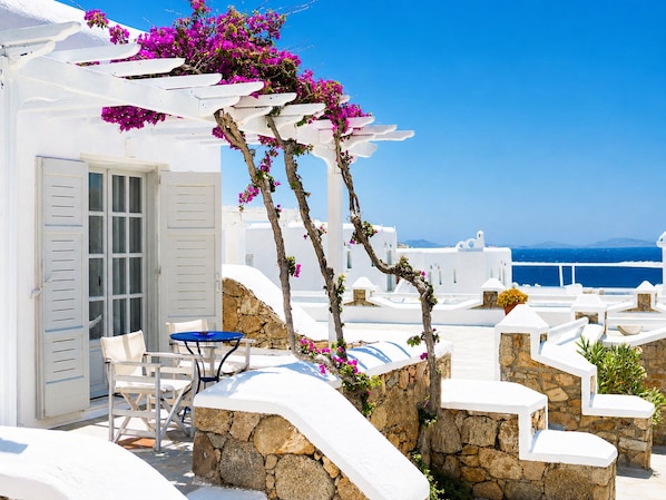 A white building with a stone wall, a blue table, and a white chair. - San Marco Hotel (Mykonos)