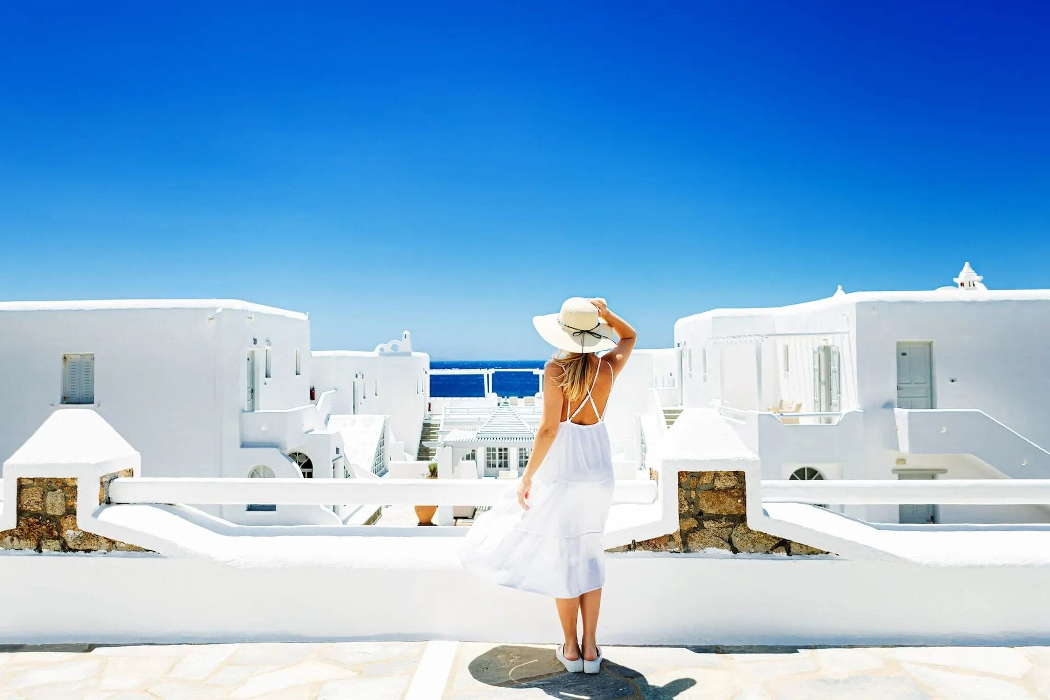 A person standing on a rooftop terrace with white buildings and a clear blue sky in the background.