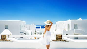 A person standing on a rooftop terrace with white buildings and a clear blue sky in the background.
