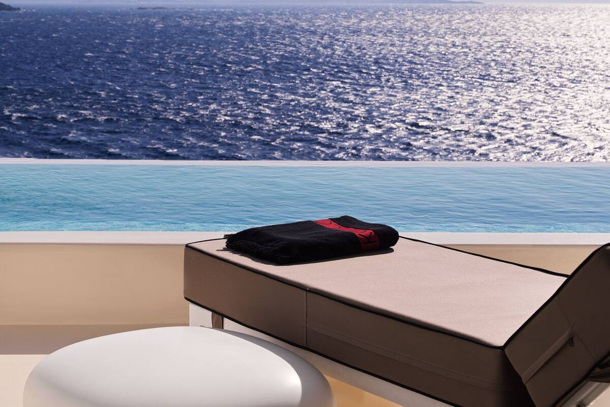 A poolside area with a lounge chair and a towel, overlooking a body of water with distant landforms.