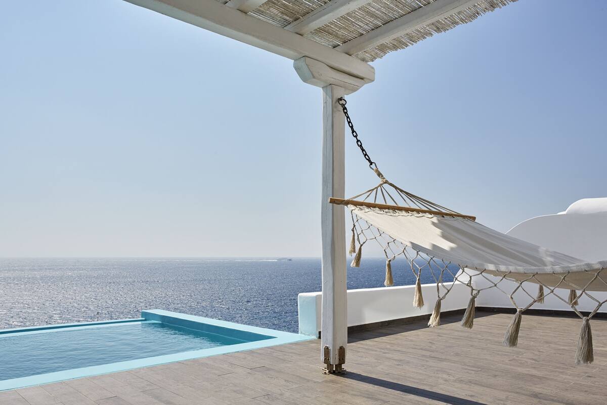A pool with a clear view of the sea, a hammock, and a white structure.